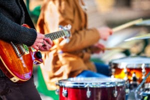 Festival music band. Hands playing on percussion instruments in park . Drums with sticks closeup. Sharpen is guitar and man hand.
